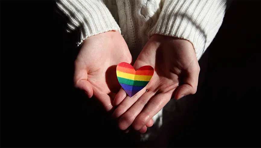two hands holding a rainbow colored paper heart