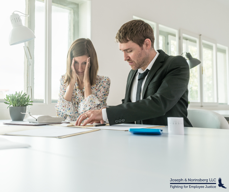 Two employees sitting at a desk with one employee visibly upset