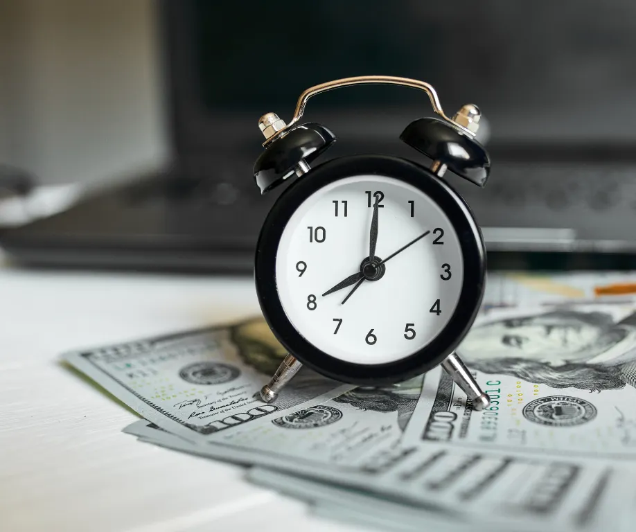 Tabletop analog clock sitting on top of fanned out $100 bills to represent wage and hour practices