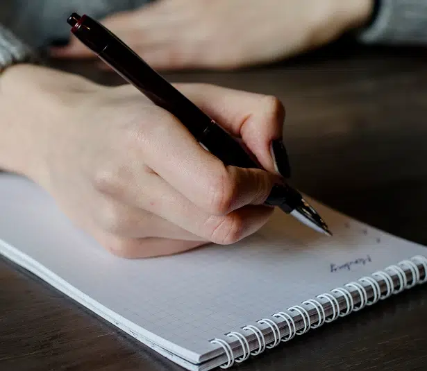 a persons hand with a pen and note pad