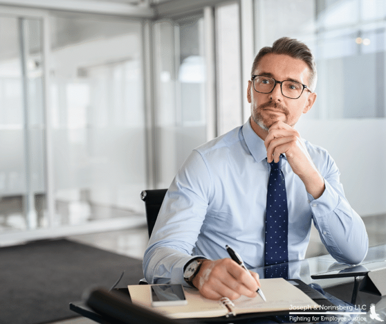Male employee at a desk dressed in business casual looking up as if deep in thought